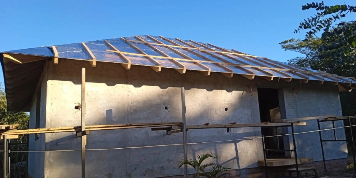 Single-story house under construction in Paraguay with wooden roof framing and concrete walls, showcasing a residential building project