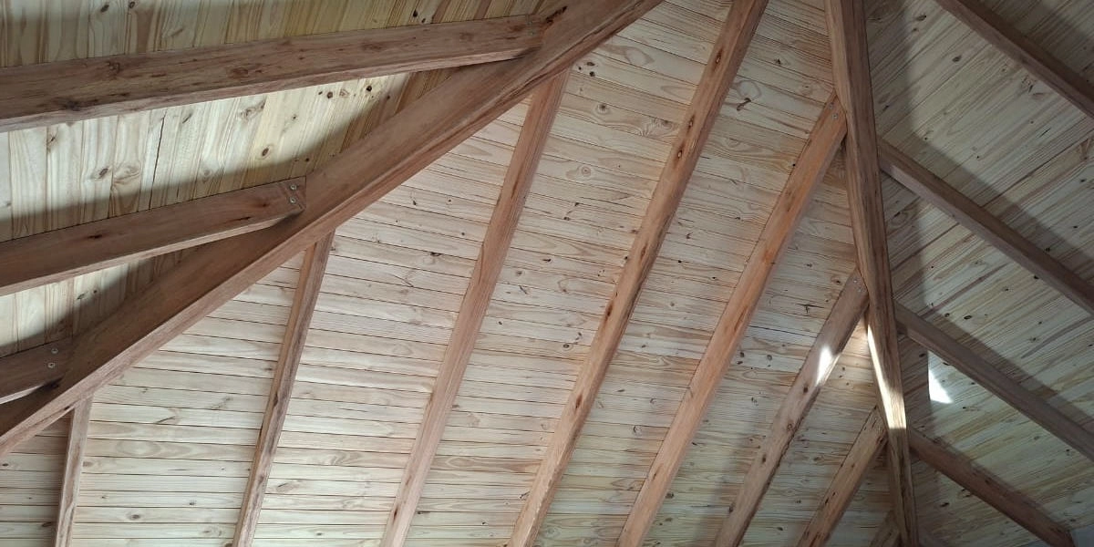 Innenansicht einer Holzdachkonstruktion mit sichtbaren Balken und Kiefernholzpaneelen, demonstriert traditionelle Dachbauweise aus Holz