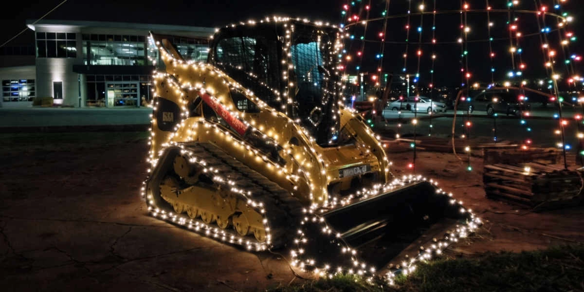 Gelber Kompaktlader mit weißen Lichterketten bei Nacht neben einem Gebäude und geparkten Autos