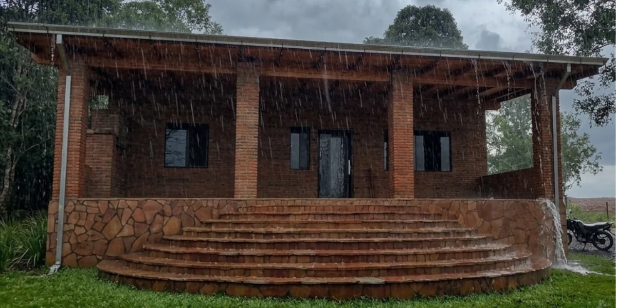 Starker Regen auf ein Ziegeldach in Paraguay mit überlaufender Dachrinne und nasser Hausfassade